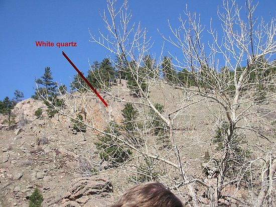White pigmatites in hillside are caused by high amounts of silica and water being injected into the rock.  The white is areas are quartz coves in the middle of the pigmatities.